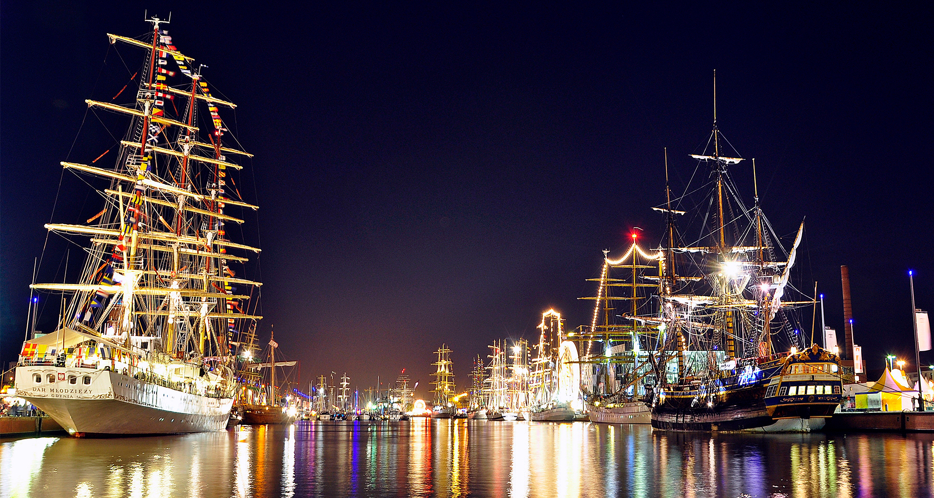 Nachtaufnahme vom Neuen Hafen mit vielen beleuchteten Segelschiffen.